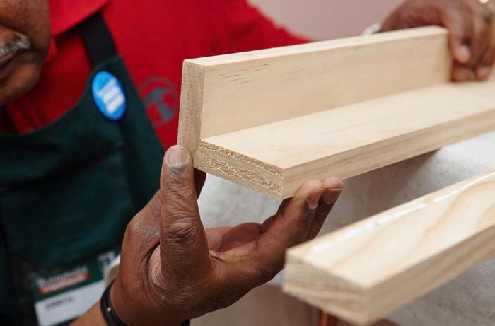 A person holding two lengths of pine timber joined to make an L shape