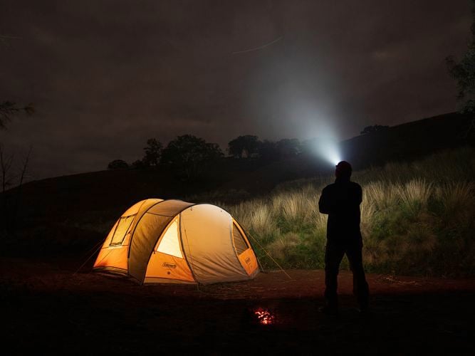 Person using light to look into night sky, tent lit up with orange glow.