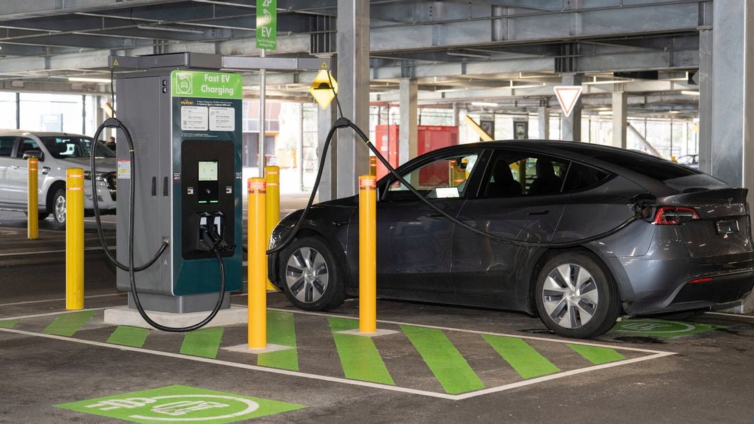How to use a public EV charging station, demonstrated by a black Tesla parked and charging at a fast EV charger in a multi-level car park.