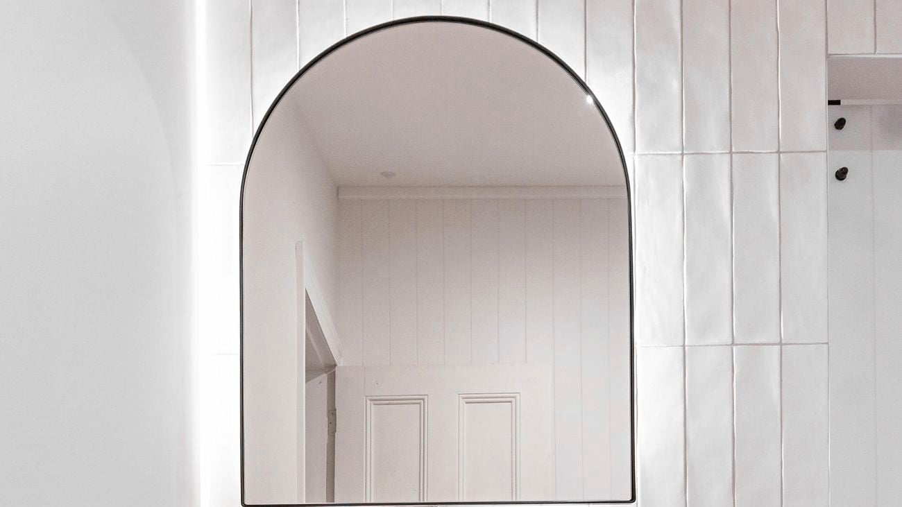 Bathroom with wooden cupboards, semicircular mirror with mirror light and white tiles