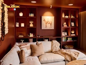 A cozy living room with a sectional sofa decorated with pillows and a blanket. Behind the sofa, built-in shelves display books, artwork, and decorative items, with a prominent horse painting at the center. The room features warm lighting and earthy tones, creating a welcoming ambiance.