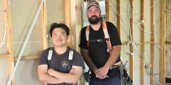 : Two tradies on a job site, one with arms crossed the other with hands in front, both smiling.
