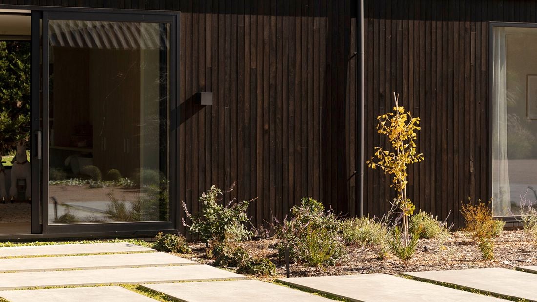 A modern house with a dark corrugated roof and landscaped garden.   