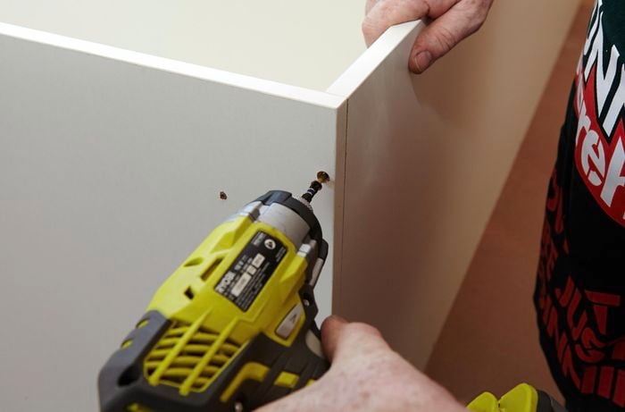 Person drilling screw into panel of pantry