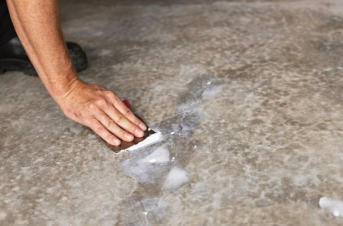 A person repairs a crack in a concrete garage floor