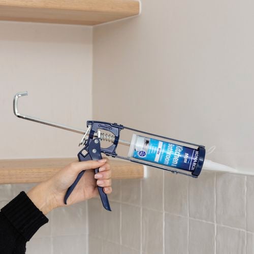 Hand using caulking gun to apply kitchen and bathroom sealant to tiles.