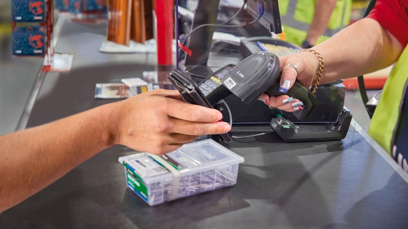 Two hands interacting at a checkout, one holding a payment terminal and wallet, the other a barcode scanner.