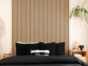 A room with floor lamp, bed and timber panels on the wall.