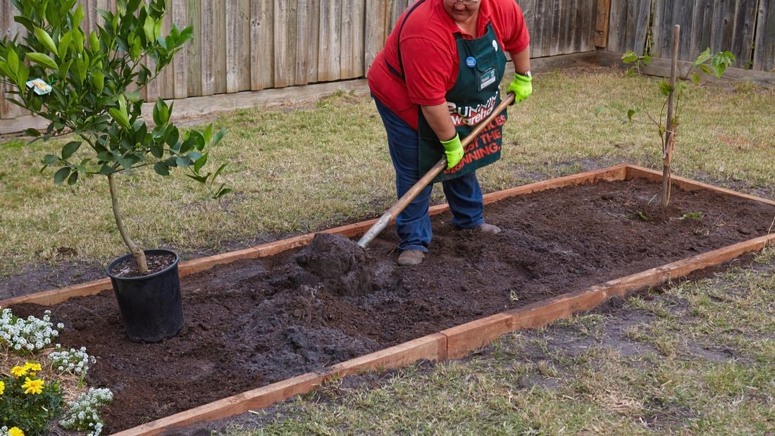 A Bunnings team member shovelling potting mix into a garden bed