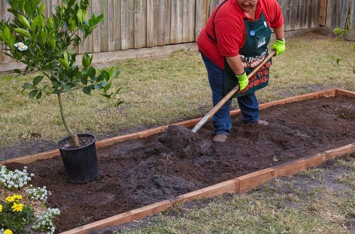 A Bunnings team member shovelling potting mix into a garden bed
