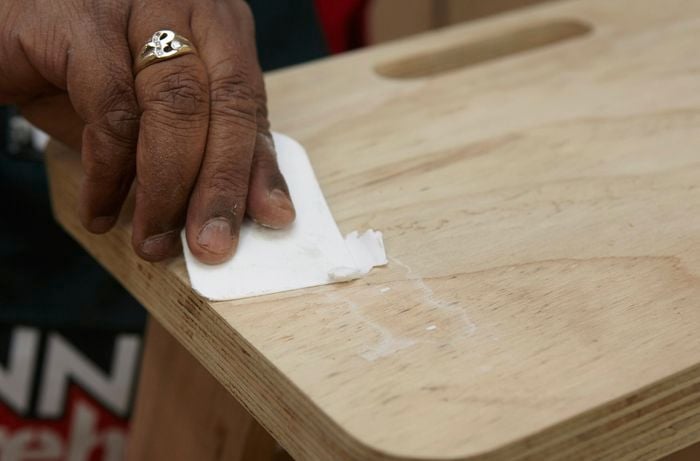 Person sanding piece of ply wood that has putty on it, that was used to fill some holes.