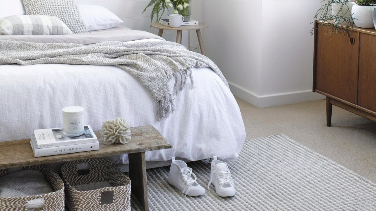 Bed with white sheets, white walls, plants in pots and brown cabinet.
