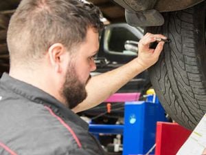 mechanic reviewing car tyres while car is on a hoist.