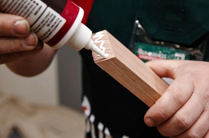 A person applying glue to the end of a piece of timber