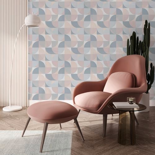 A blush pink chair with geometric wallpaper in the background.