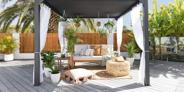 Outdoor gazebo styled with cushions, couch, hanging baskets and sheer curtains.