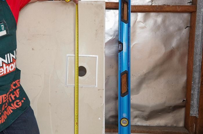 Measuring the width and length of a shower sump along a floor sheet, along with a spirit level used to align the sump