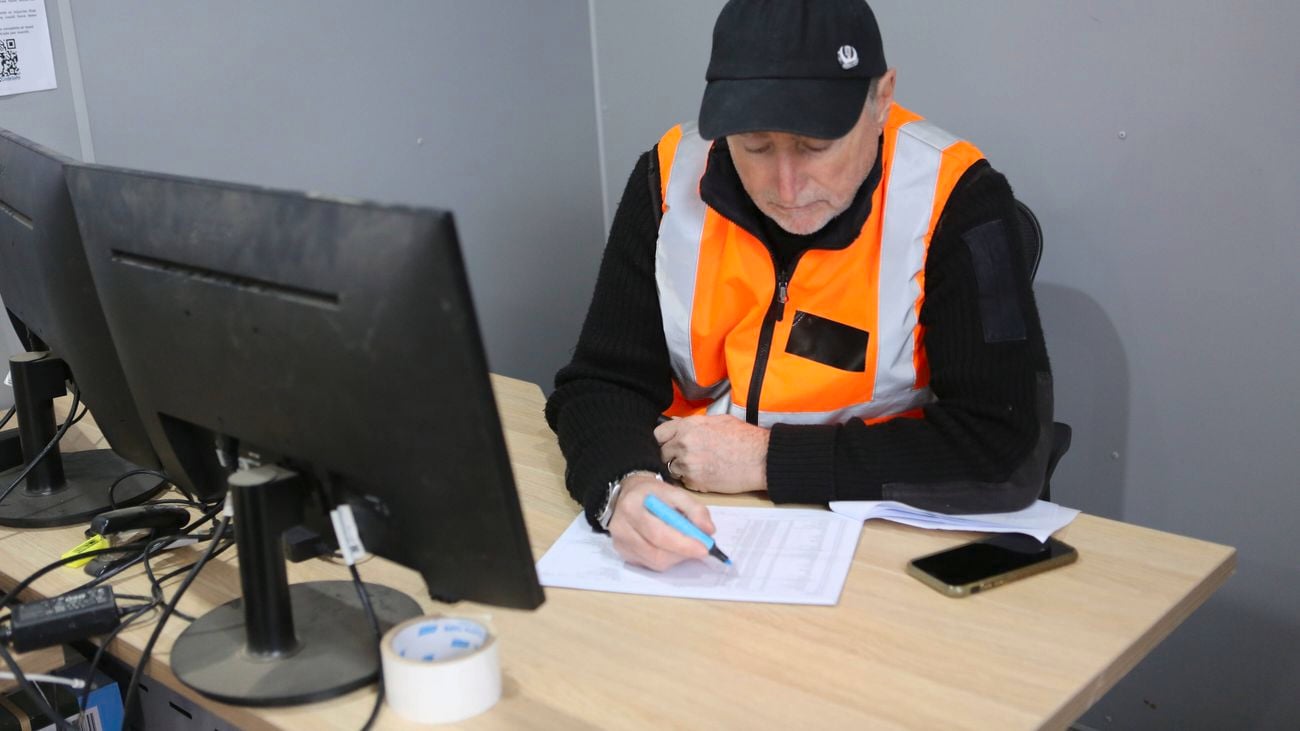 A site foreman wearing hi-vis sits at his desk in his office doing paper work while holding a highlighte