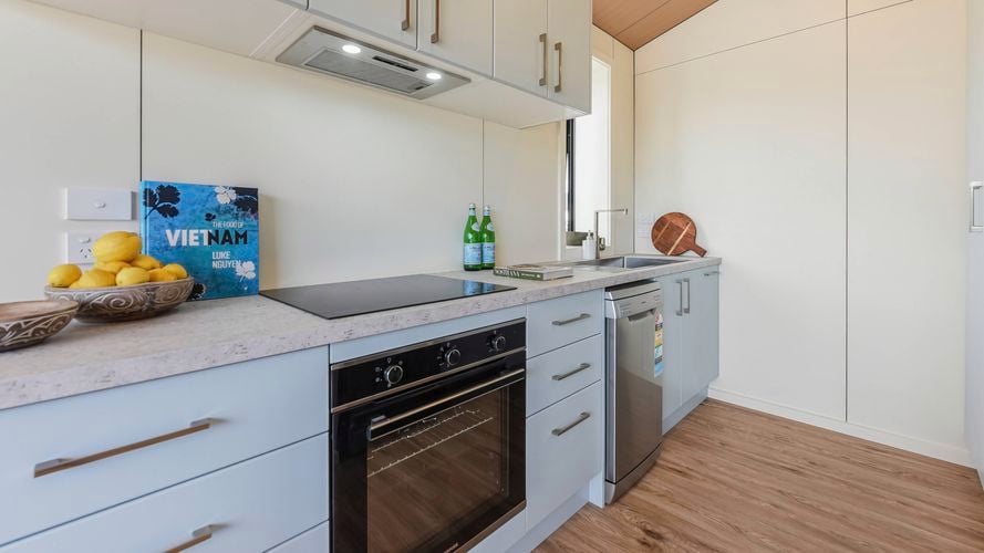 Modern granny flat kitchen with light cabinetry, built-in oven, cooktop and compact laundry.