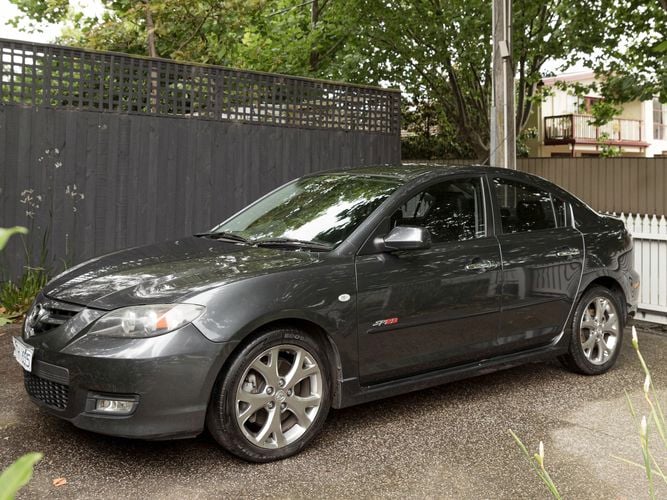 A steel grey Mazda SP23 is parked in the shade of a tree.
