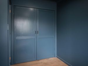 Image of a wardrobe with two doors, painted in a deep shade of navy blue, with a smooth and glossy finish.