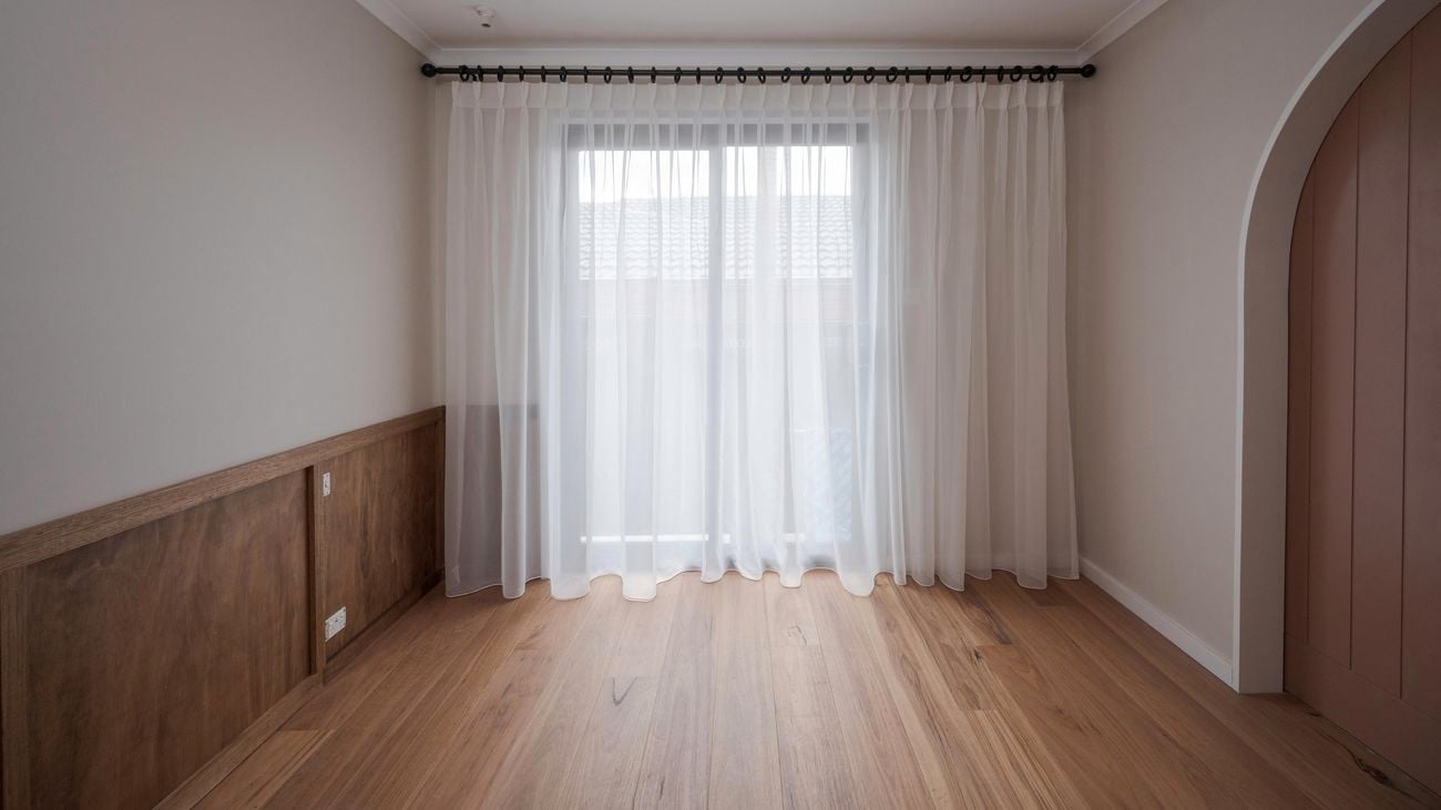 Lounge room with white walls and large window at the end of the room with sheer curtains