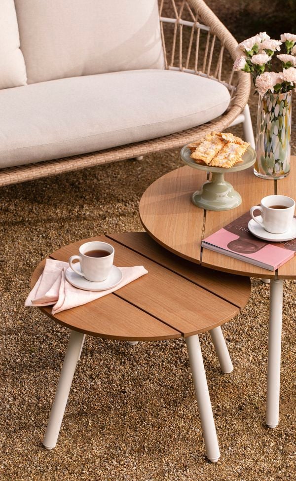 Brown timber outdoor tables with crockery on them and an lounge chair outside.