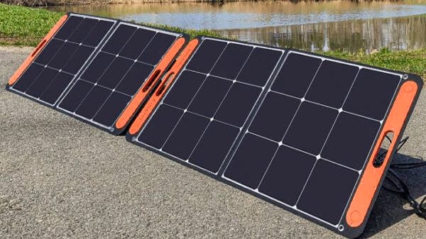 Foldable Jackery solar panels are set up on a paved surface near a grassy area and a pond.]