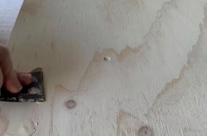 Hands using sanding tool to smooth over plywood.