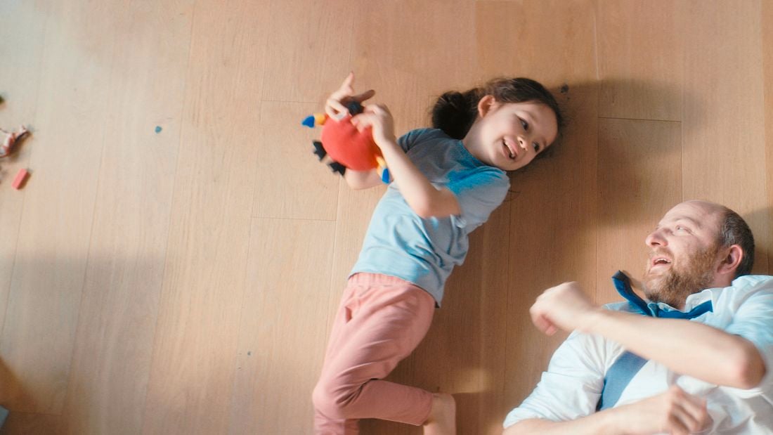 A father and daughter play together on the floor.