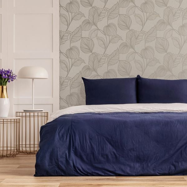 A bedroom with a Boutique wallpaper wall and a table, vase next to the bed.
