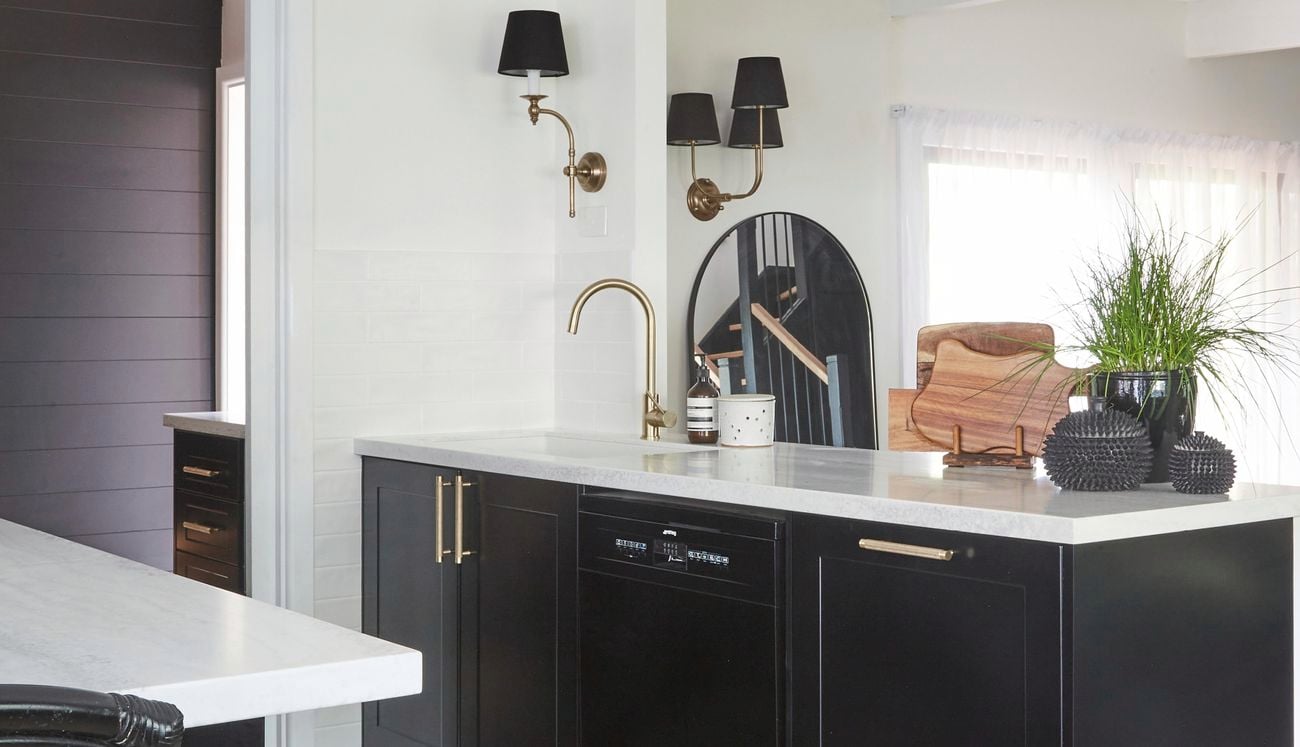 Modern kitchen with black cabinetry, gold tapware, white marble benchtop and white walls.
