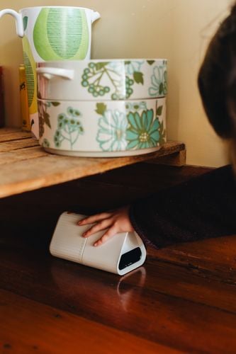 A smart mouse trap being placed indoors under a shelf