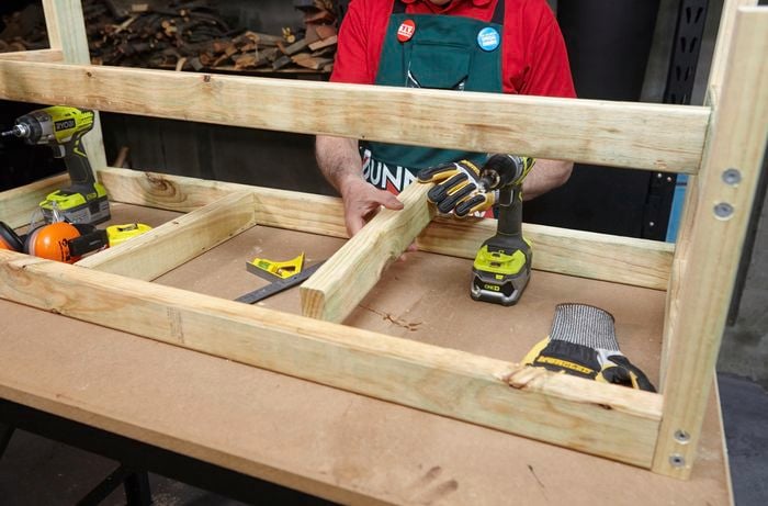 Person assembling wooden garden bench frame.