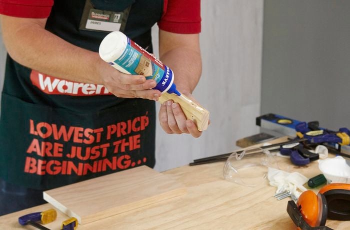 A person applying glue to a small piece of wood
