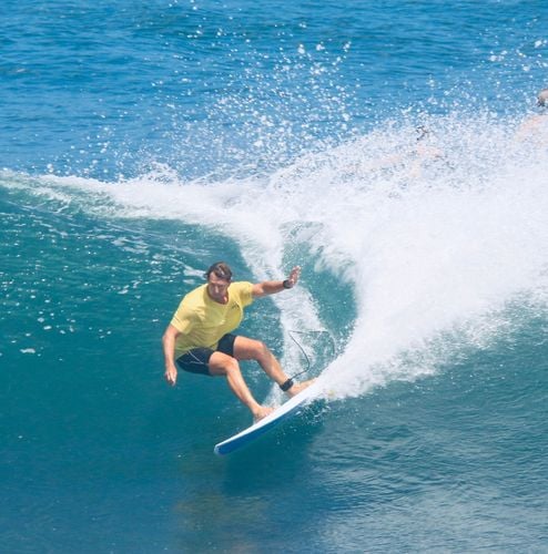 Surfer in a yellow shirt carving a turn on a white Summer vibes surfboard.