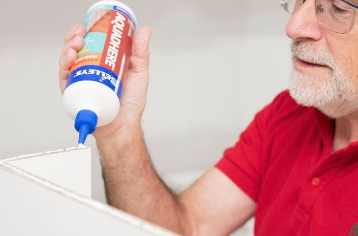 Build the drawer base by applying woodworking glue to the edge of a cabinet panel 