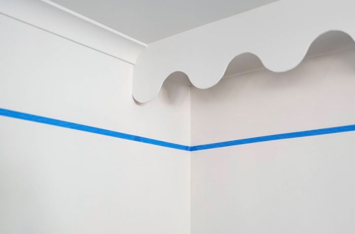 A painter’s tape is carefully placed around the corner of the wall to define the colour-cap line before painting. 