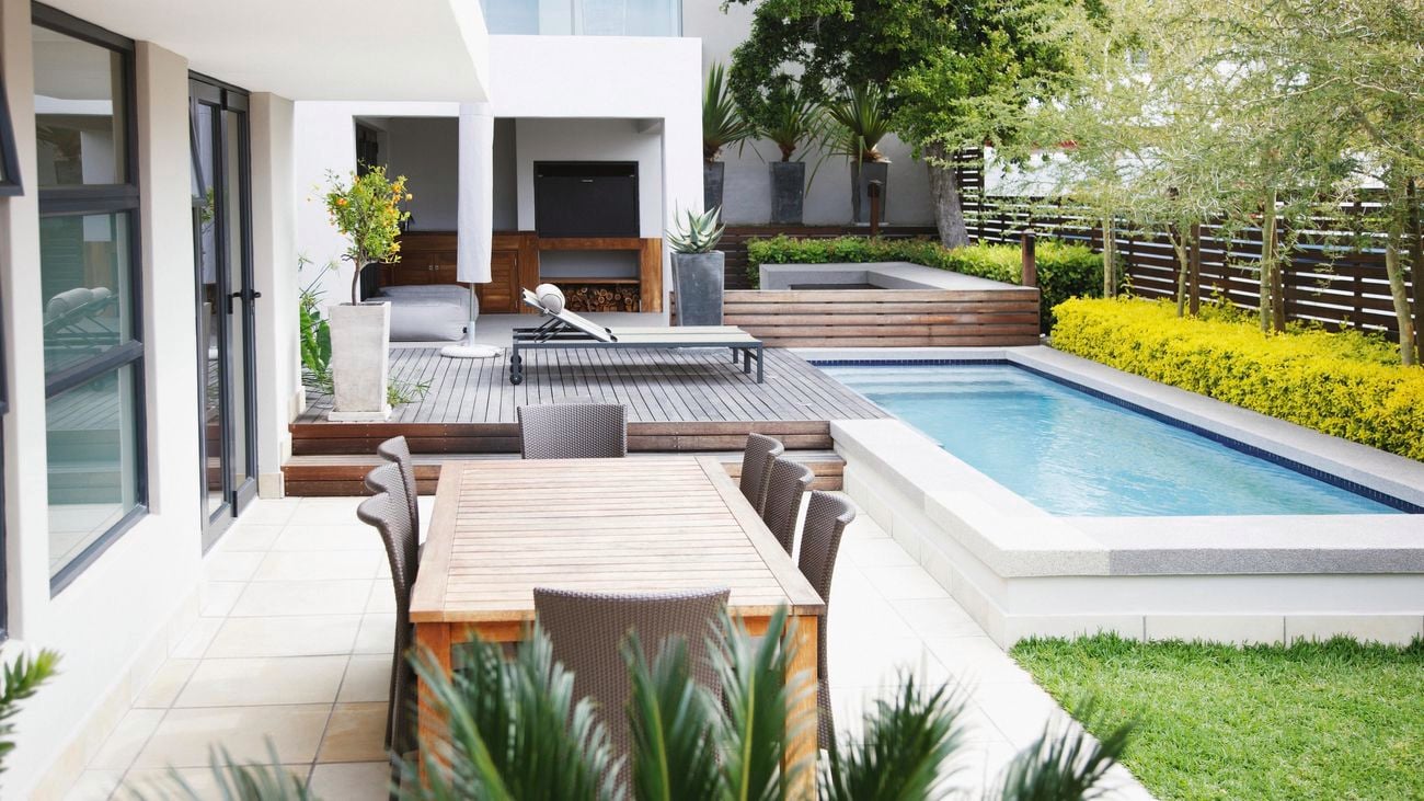 Backyard featuring lawn, tiled area with outdoor table setting, decking and pool.