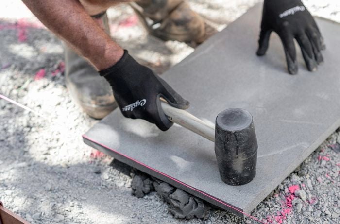 Person wearing work gloves tapping a paving stone placed on top of mortar with a rubber mallet.