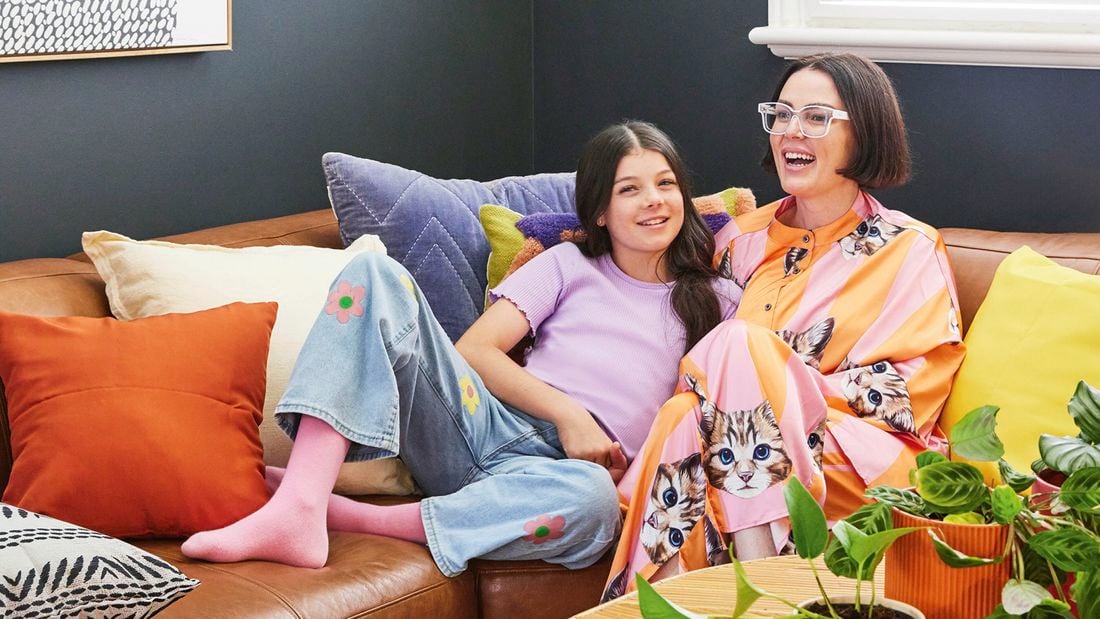 Happy pair lounging on tan leather sofa with colourful pillows in a neurodivergent design space featuring contrasting dark walls, varied textures, and vibrant sensory-friendly elements