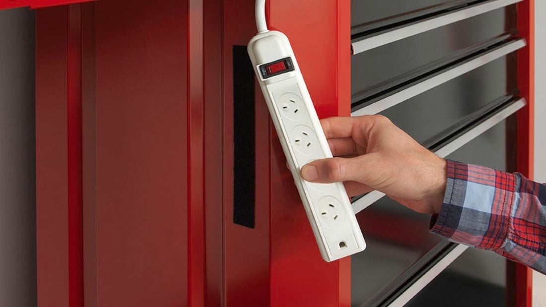 Hand holding a white power board showing a black strip of VELCRO® attached to a red bench