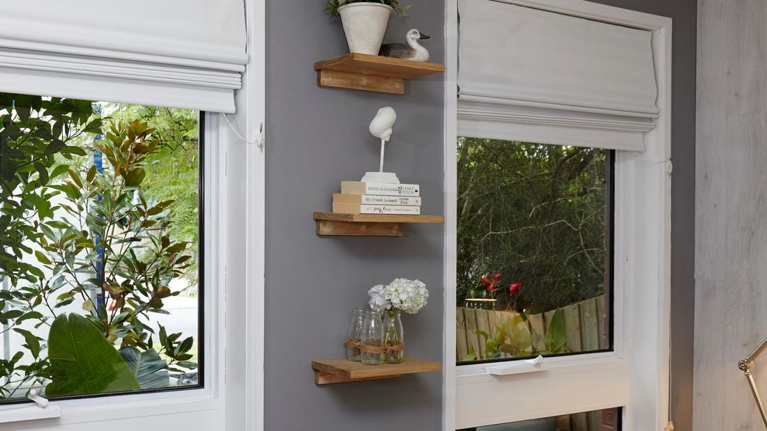Three small timber shelves arranged vertically between two windows