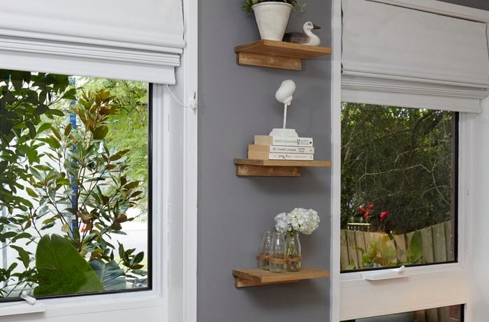 Three small timber shelves arranged vertically between two windows