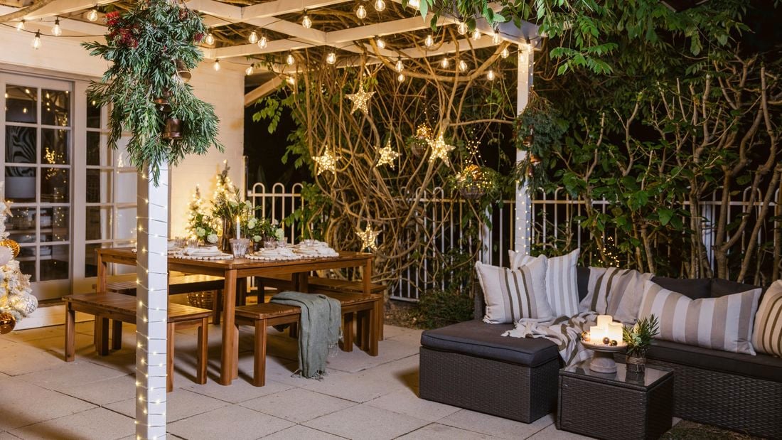 Outdoor patio decorated with string lights, wooden dining table, and cushioned seating under a pergola.
