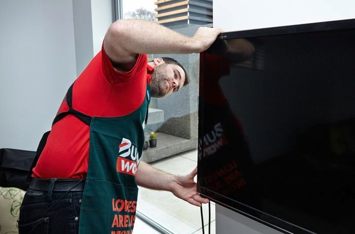 Person looking behind TV attached to the wall.