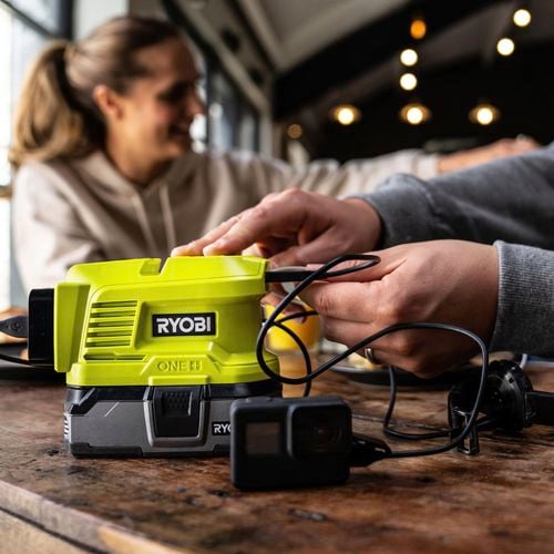 A battery topper inverter placed on a table with a charging cable plugged into it.