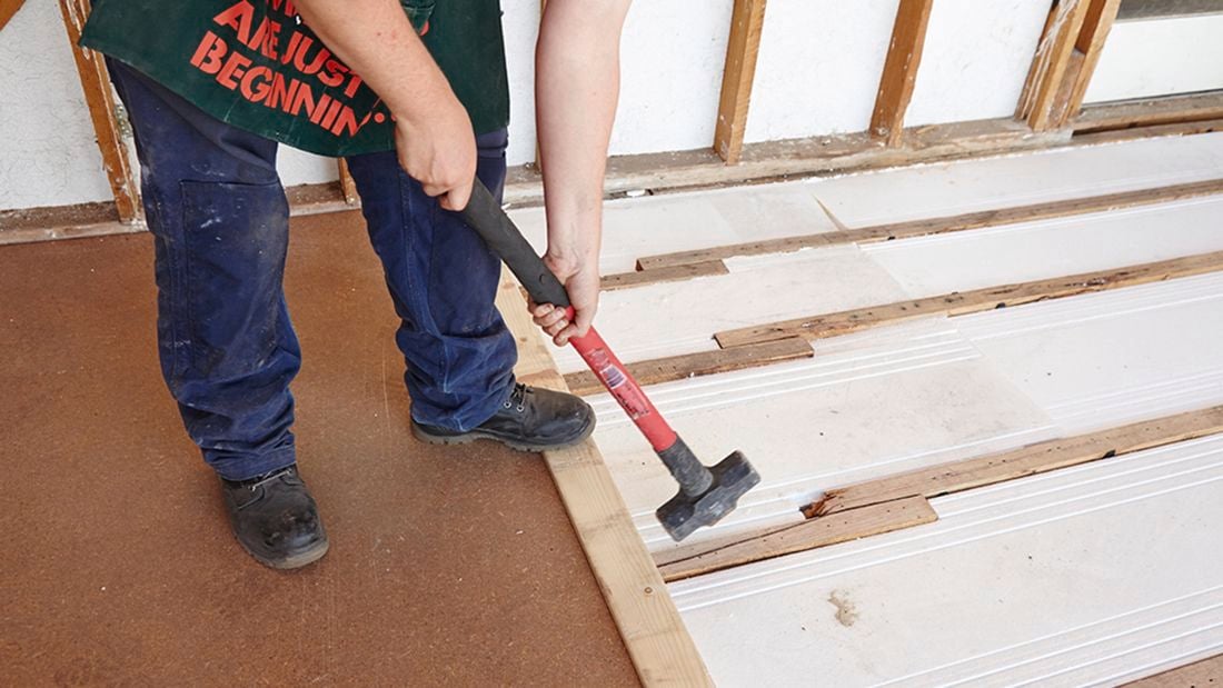 A hammer being used to hit a piece of chipboard into place