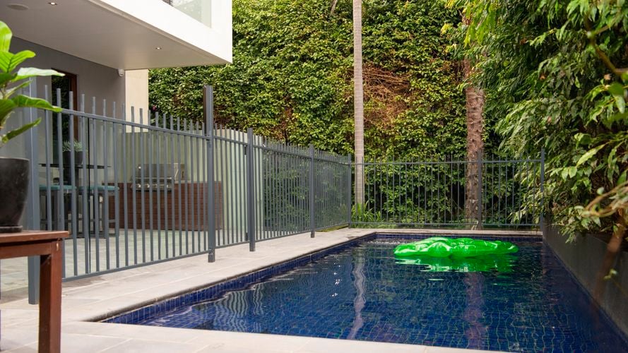 A fence surrounding a pool with a crocodile floating toy in the water.