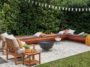 Timber lounge setting with cushions on it, chairs and a fire pit outside on pebbles.